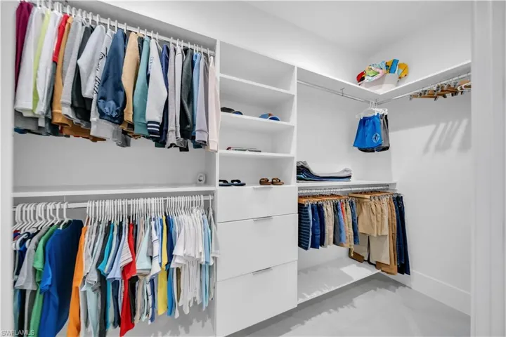 Custom white built-in closet system featuring multiple hanging rods, open shelving, and integrated drawers