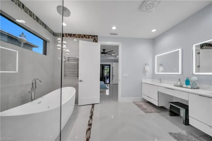 Spacious bathroom featuring a freestanding soaking tub, clear glass shower enclosure, dual vanity with undermount sinks, and illuminated mirrors