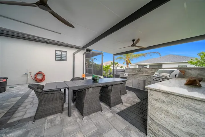 Behind RV Garage Covered outdoor patio featuring extensive paver flooring, a built-in outdoor kitchen with grill, and two ceiling fans