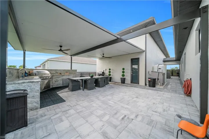 behind RV Garage Expansive paver patio featuring a built-in outdoor kitchen with grill, covered ceiling with integrated fans, and contemporary exterior architecture