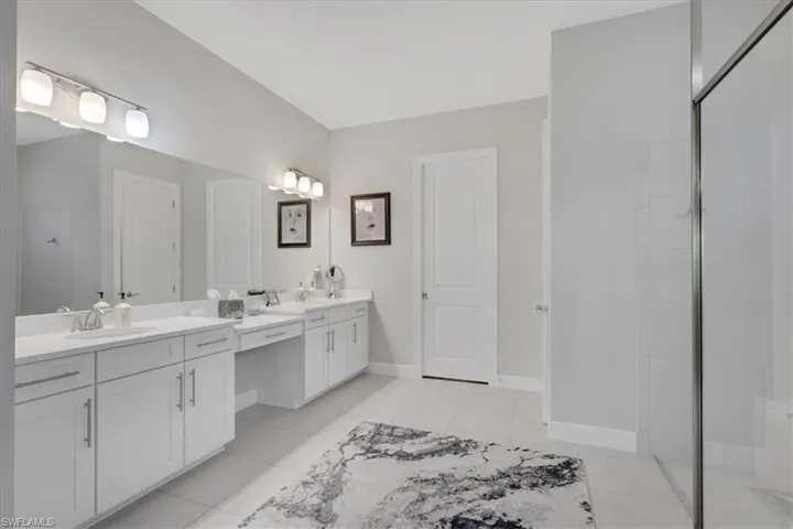 Full bath with two vanities, a shower stall, and light tile patterned floors