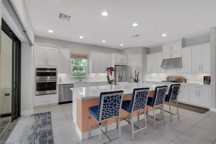 Kitchen with a breakfast bar area, stainless steel appliances, a center island, white cabinetry, and under cabinet range hood
