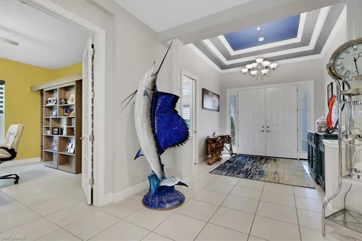 Entrance foyer with a raised ceiling, a chandelier, crown molding, and light tile patterned floors