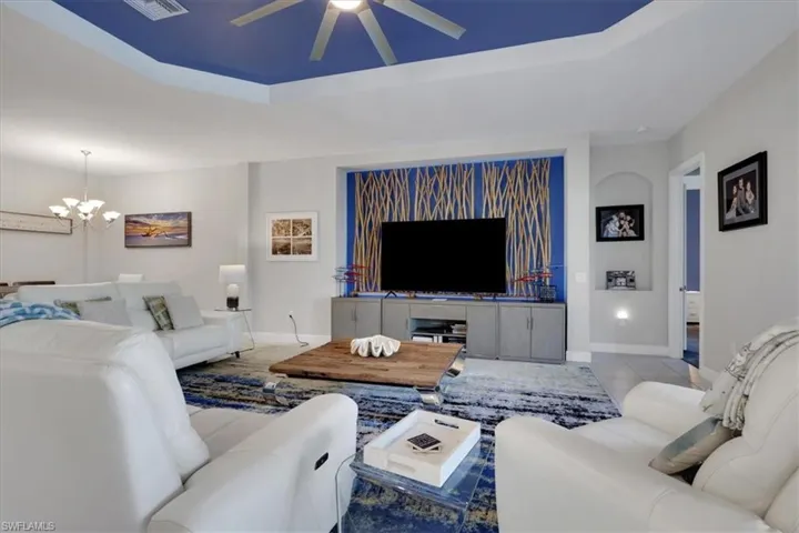 Tiled living room featuring a raised ceiling, a chandelier, and ceiling fan