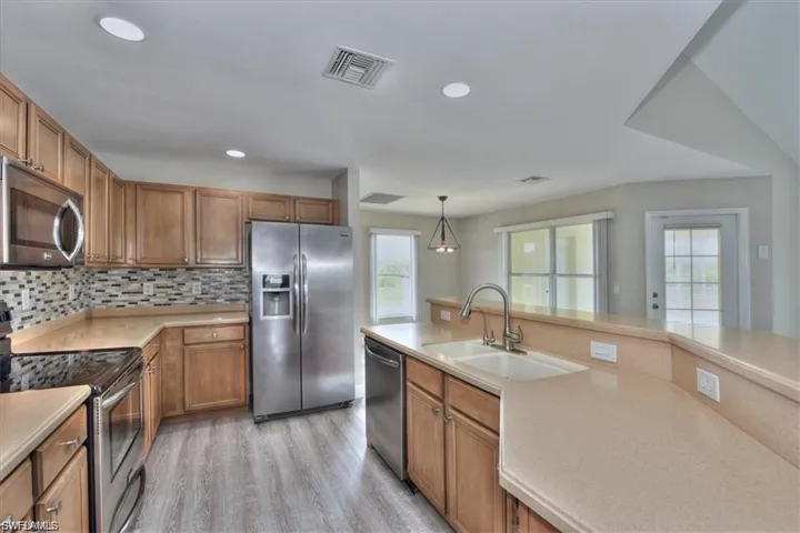Kitchen featuring appliances with stainless steel finishes, light wood-type flooring, backsplash, sink, and hanging light fixtures