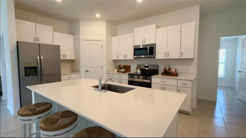 Kitchen with white cabinetry, light tile patterned flooring, appliances with stainless steel finishes, a center island with sink, and recessed lighting