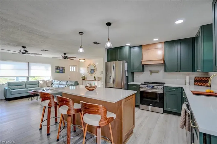 Kitchen featuring a breakfast bar, backsplash, premium range hood, ceiling fan, and appliances with stainless steel finishes