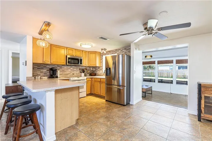 Kitchen with kitchen peninsula, appliances with stainless steel finishes, a kitchen breakfast bar, tasteful backsplash, and ceiling fan