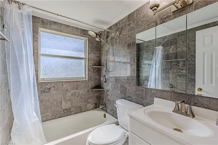 Full bathroom with vanity, toilet, ornamental molding, tile walls, and shower / tub combo with curtain