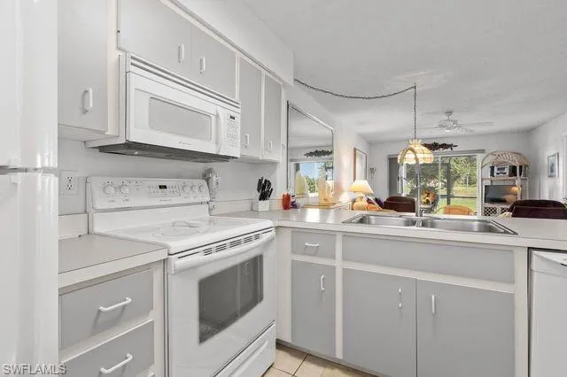 Kitchen featuring white appliances, pendant lighting, sink, ceiling fan, and light tile floors