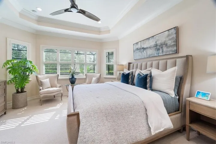 Carpeted bedroom with a raised ceiling, a ceiling fan, and crown molding