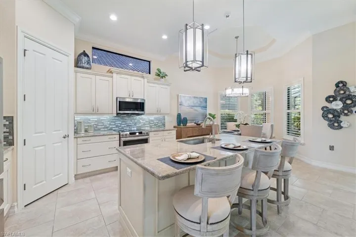 Kitchen with light stone counters, a sink, appliances with stainless steel finishes, an island with sink, and decorative light fixtures