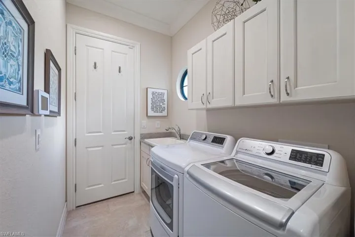 Washroom with ornamental molding, cabinet space, a sink, and washing machine and clothes dryer
