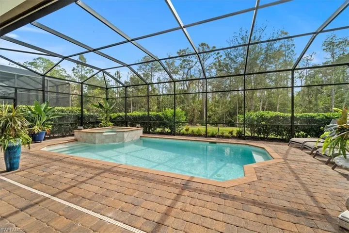 View of swimming pool featuring glass enclosure, a pool with connected hot tub, and a patio