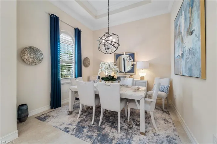 Dining area featuring a tray ceiling, a notable chandelier, light tile patterned floors, ornamental molding, and baseboards