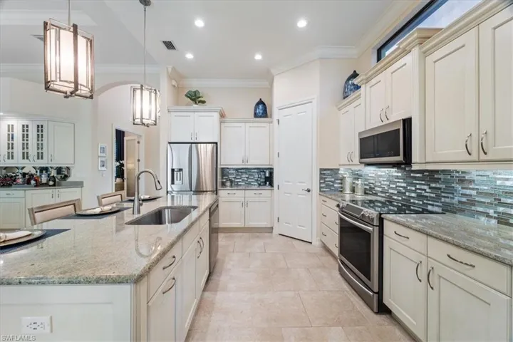 Kitchen with a center island with sink, appliances with stainless steel finishes, ornamental molding, hanging light fixtures, and a sink