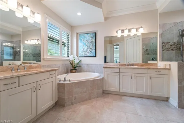 Full bath featuring a garden tub, crown molding, two vanities, a stall shower, and a sink