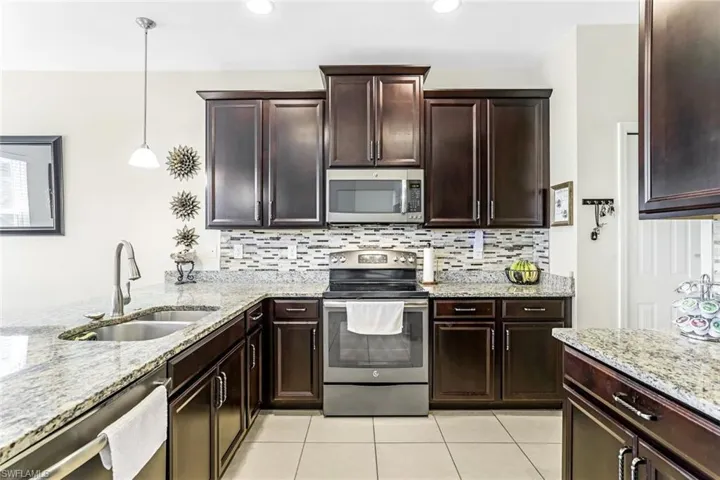 Kitchen with light tile patterned flooring, sink, stainless steel appliances, and decorative backsplash