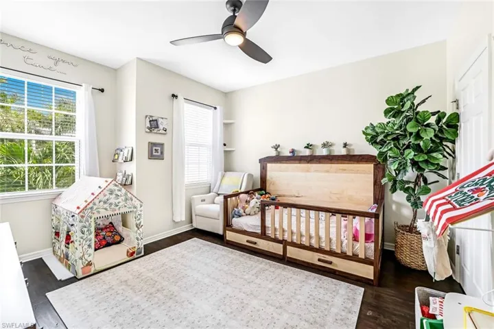 Bedroom with dark hardwood / wood-style flooring, a crib, multiple windows, and ceiling fan