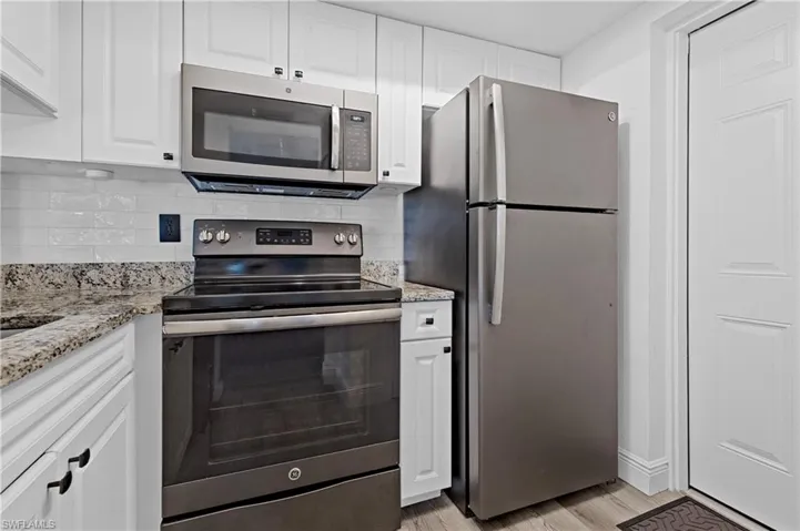 Kitchen featuring stainless steel appliances, white cabinetry, decorative backsplash, and light stone counters