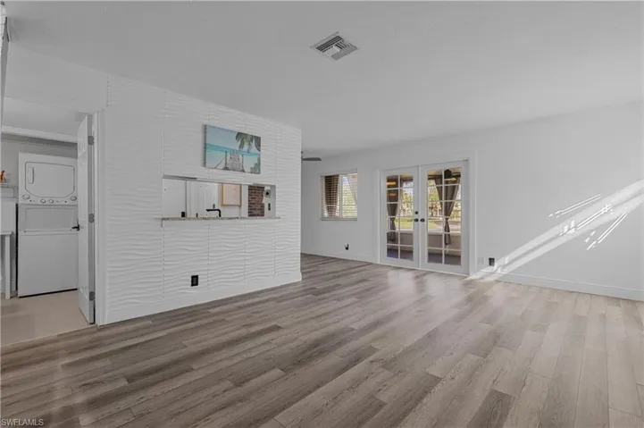 Unfurnished living room featuring french doors, light wood-type flooring, and stacked washing machine and dryer