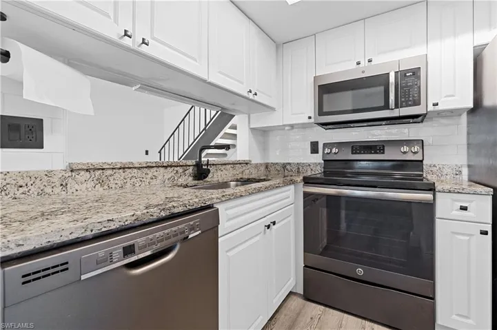 Kitchen with stainless steel appliances, light stone countertops, white cabinetry, tasteful backsplash, and light wood-type flooring