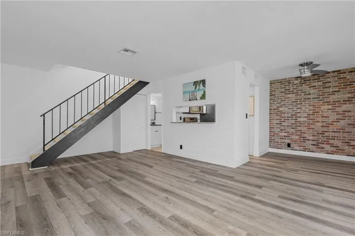 Unfurnished living room with brick wall, light wood-style flooring, stairway, and ceiling fan