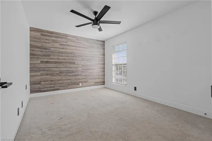 Spare room featuring wood walls, light colored carpet, an accent wall, and ceiling fan