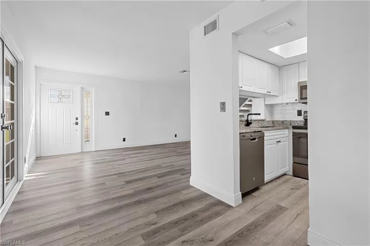 Kitchen with white cabinets, stainless steel appliances, a skylight, light stone countertops, and light wood finished floors