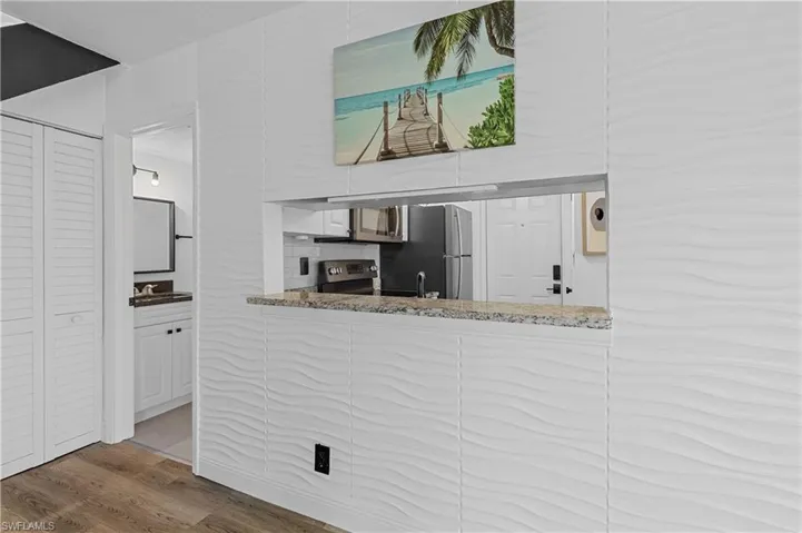 Kitchen with light stone countertops, wood finished floors, stainless steel range with electric stovetop, and white cabinetry