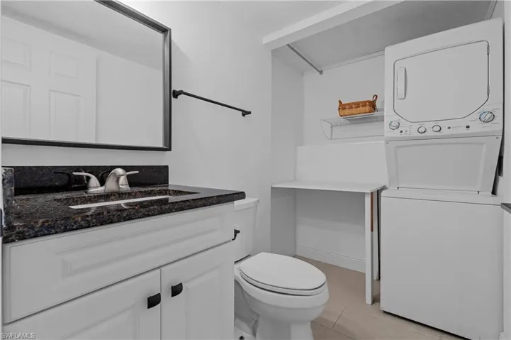 Half bathroom featuring vanity, stacked washer and clothes dryer, and light tile patterned floors