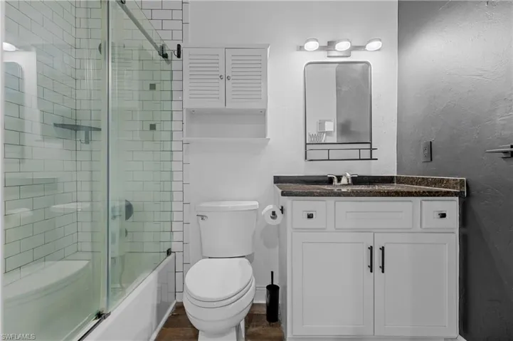 Bathroom with vanity, bath / shower combo with glass door, and dark wood-style floors