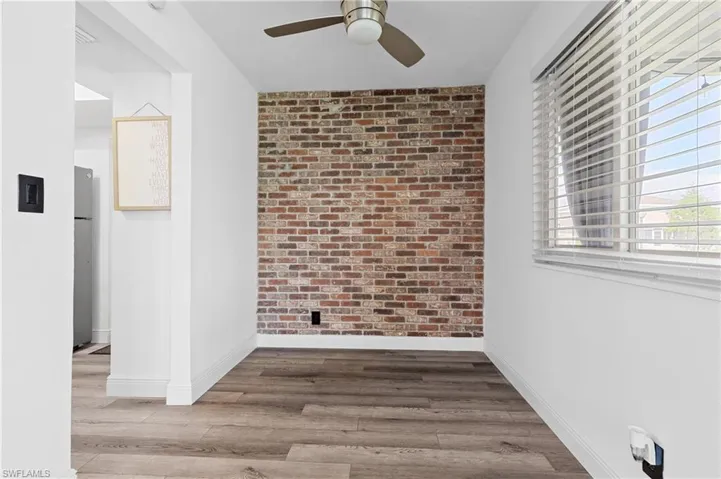 Spare room featuring brick wall, light wood finished floors, and ceiling fan