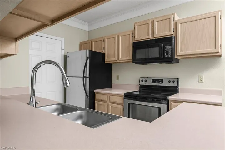 Kitchen featuring light wood finish cabinets, stainless steel appliances, light countertops, and ornamental molding