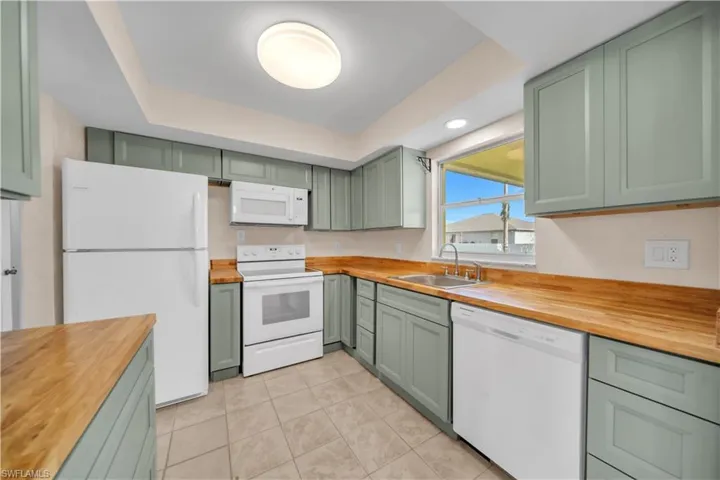 Kitchen featuring wood-finish countertops, white appliances, sage green cabinetry, a double basin stainless steel sink, and ceramic tile flooring