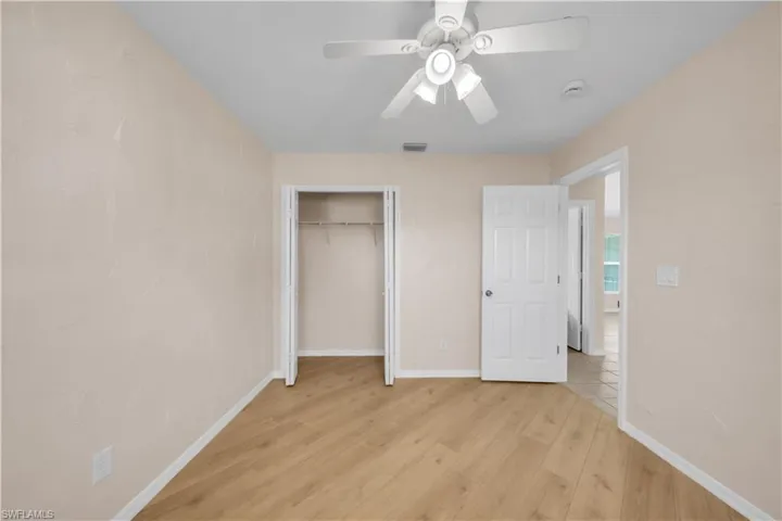 Bright room featuring light-toned walls, wood-finish flooring, a ceiling fan with integrated lighting, and a closet with bifold doors