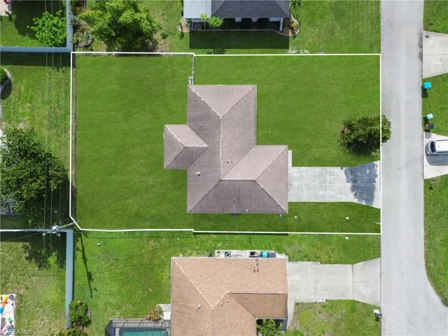 Aerial view showcasing a residential property with a central house, expansive green lawn, and a concrete driveway