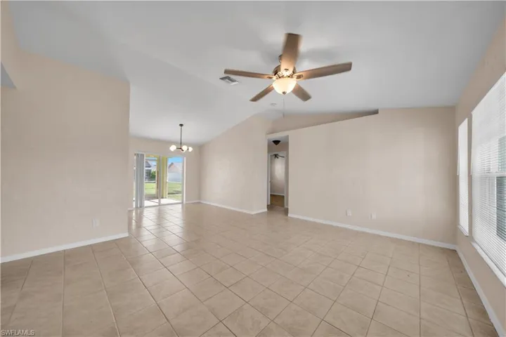 Spacious living area featuring neutral tile flooring, vaulted ceilings, and a ceiling fan with integrated lighting