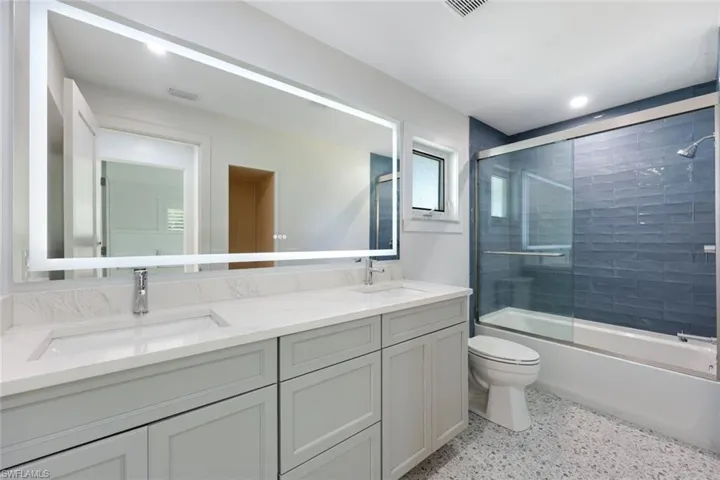Bathroom with double vanity, combined bath / shower with glass door, speckled floor, and recessed lighting