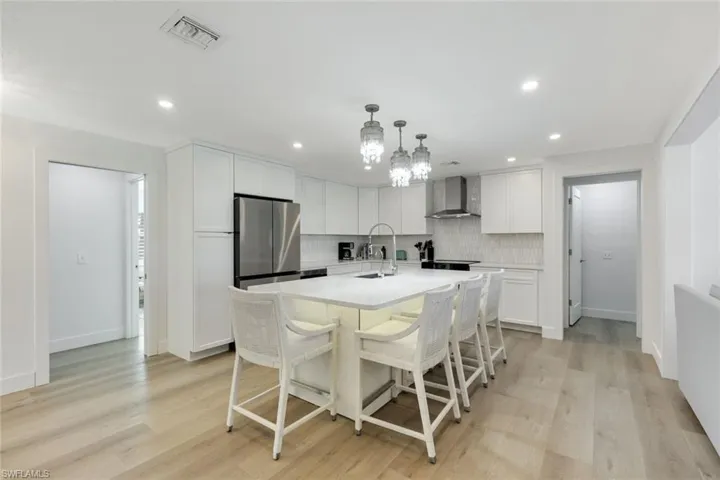 Kitchen with backsplash, light countertops, freestanding refrigerator, a kitchen breakfast bar, and light wood-style floors