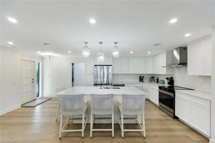 Kitchen featuring stainless steel appliances, decorative backsplash, wall chimney exhaust hood, light countertops, and a center island with sink