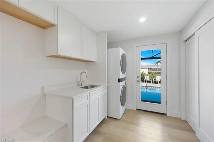 Washroom featuring stacked washing machine and dryer, light wood finished floors, and cabinet space