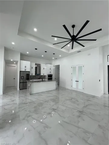 Unfurnished living room with ceiling fan, sink, a tray ceiling, and light tile floors