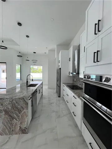 Kitchen with double oven, sink, white cabinetry, and pendant lighting