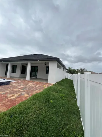 View of side of property with ceiling fan, a lawn, and a patio