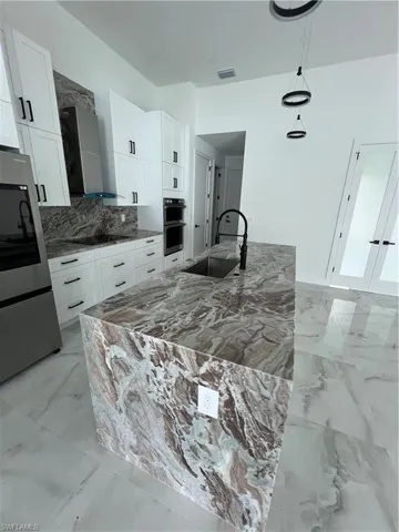 Kitchen featuring double wall oven, ventilation hood, decorative light fixtures, light tile floors, and sink