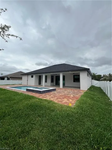 Rear view of house featuring a patio, a pool with hot tub, and a lawn