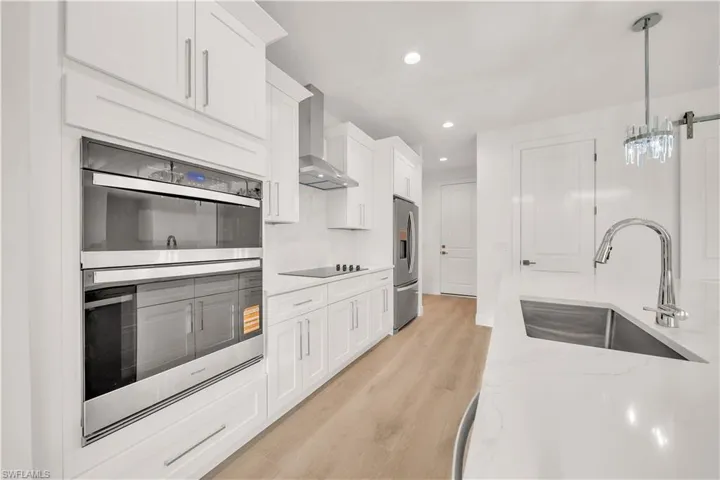 Modern kitchen featuring white cabinetry, stainless steel appliances, light-toned wood-finish flooring, and a crystal-detail pendant light