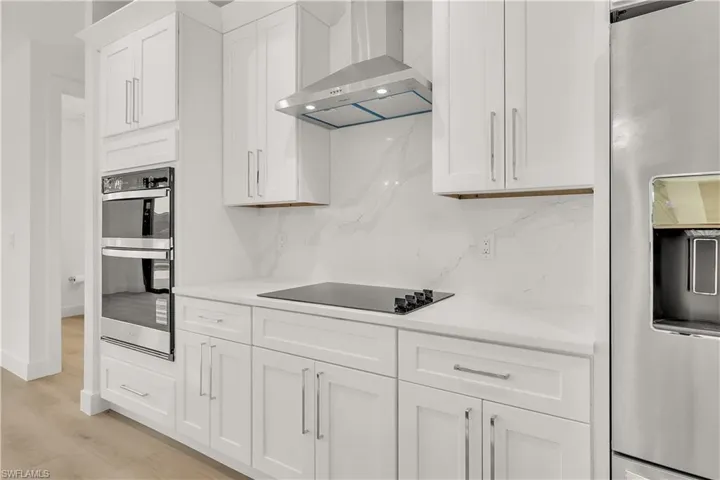 Contemporary kitchen featuring white cabinetry, integrated double ovens, a built-in cooktop, and a stainless steel refrigerator