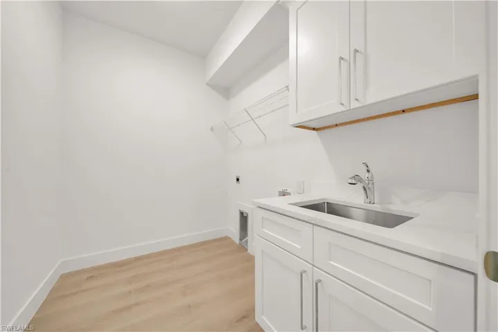 White cabinetry with chrome hardware, an undermount stainless steel sink, a chrome pull-down faucet, and wood-finish flooring